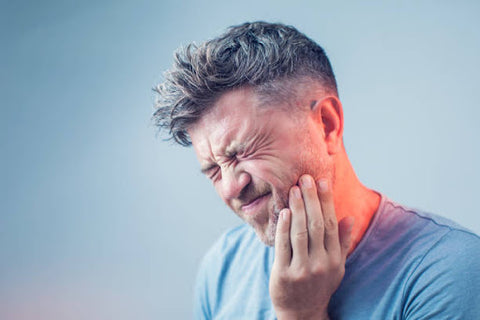 Homme souffrant, la main sur la joue, indiquant un mal de dents.