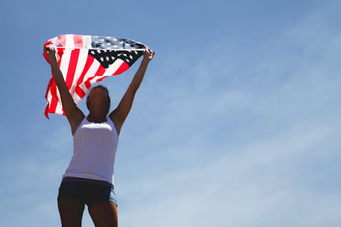 Femme tenant un drapeau américain au-dessus de sa tête avec un ciel bleu en arrière-plan.